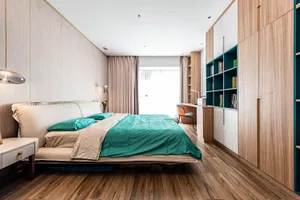A modern bedroom featuring a wooden bed with teal bedding and a bookshelf in the background.