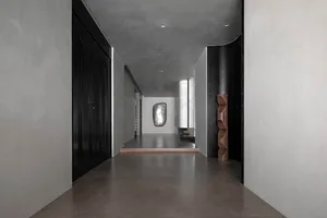 Modern interior design featuring a corridor with concrete flooring and walls, minimalist art, and wooden sculpture.