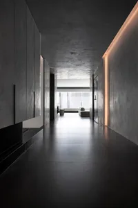 A modern corridor with concrete walls and floor, featuring a minimalist design and soft lighting along the ceiling.