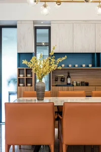 A modern dining room featuring wooden furniture and glass elements, with a vase of yellow flowers on the table.