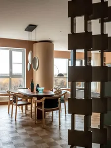 Modern dining room with wooden floor, wooden chairs, and a round dining table with decorative glass objects.