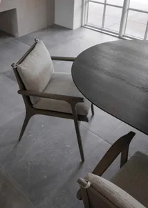 Modern dining room with a round wooden table and upholstered chairs with light-colored cushions.