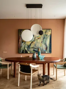 A modern dining room featuring a wooden table surrounded by chairs, a hanging light fixture, and a colorful painting on the w