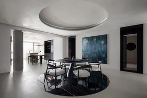 Circular modern interior featuring a black marble dining table with white chairs, white walls, and a large blue abstract pain