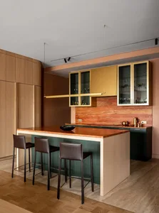 A modern kitchen featuring a wooden island with three bar stools, and cabinets with glass doors.