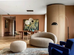 A modern living space featuring a white circular sofa, white footstool, and wooden flooring.