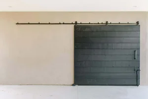 A modern, minimalist barn door wall featuring a horizontal black slat wall on a beige wall with a black metal rail mounted ab