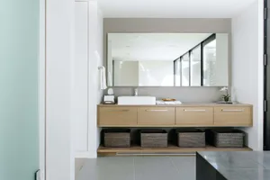 Modern minimalist bathroom featuring a wood vanity with storage baskets, a white sink, and a large mirror.
