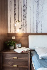A modern minimalist bedroom featuring a wooden bed frame and nightstand with a potted plant, an open book, and a spherical pe