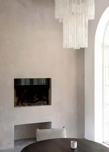 A minimalist living room featuring a concrete fireplace, a chandelier, and a round table.
