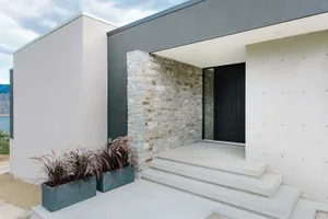 Modern minimalist front entrance featuring a stone wall and concrete steps.