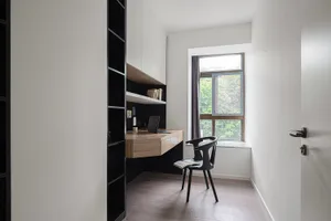A minimalist home office featuring a wooden desk and glass window, with a black chair and open book.