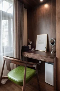 A modern workstation featuring a wooden desk with a green cushioned chair, a framed sheet of paper, and a round mirror, place