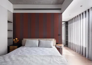 A minimalist bedroom with a striped accent wall, white bedding, and sheer curtains.