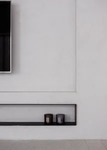 A minimalist interior with a concrete floating shelf holding two candles.