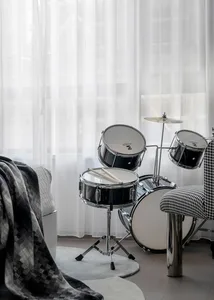 A minimalist music room with a black drum set against a white sheer curtain background.
