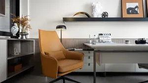 A modern home office featuring a brown leather swivel chair, a sleek white desk, and decorative elements on a floating shelf.