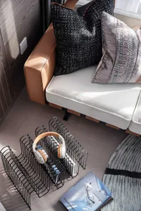 A modern living room with a sleek, minimalist sofa, textured pillows, and a wire magazine rack holding headphones and books.