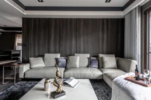 Modern living room with a grey leather sofa, wooden accent wall, and a marble coffee table with decorative items.