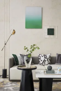 A modern living room featuring a white sofa with green and black pillows, a black side table with a vase and greenery, and a 