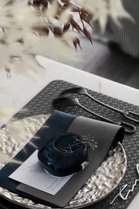 Modern table setting featuring a metallic glass vase and cloth napkin on a textured plate with a black woven placemat and cut