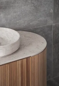 A modern bathroom with a round marble basin and wooden cabinet.