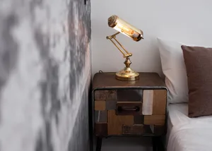 A stylish, industrial-style bedside table made of metal and wood, featuring a unique task light with an exposed bulb.