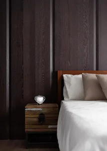 A modern industrial bedroom with wooden walls, bed, and nightstand with a vintage-style clock.