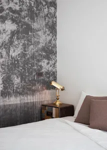 Minimalist hotel room featuring a textured wallpaper wall and a brass table lamp on a wooden bedside table.