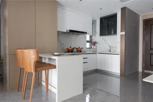 Modern kitchen with marble countertops, white cabinets, and orange pots on the stove.