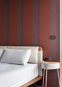 A modern minimalist bedroom with a bed, white sheets, and striped wallpaper on the walls.