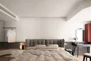 A minimalist bedroom with a textured fabric headboard and neutral bedding.