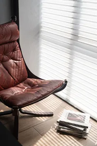 A modern lounge chair made of brown leather and featuring a wooden frame, positioned in a living room with a stack of books a