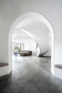 A modern living room with concrete and plaster walls and a spiral staircase.