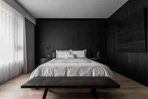 Modern minimalist bedroom featuring a dark wood bed with a white bedding set, a black leather ottoman, and dark wood paneling