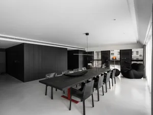 A minimalist dining room with a long, dark table and black chairs against a white floor and black wooden walls.