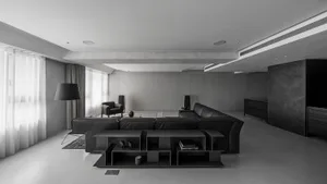 A minimalist living room with black furniture, concrete walls, and a large floor lamp.