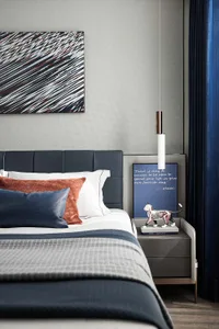 A modern bedroom with a bed adorned with various coloful pillows and blankets, a blue and white striped painting above it, a 