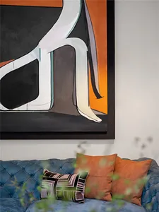A modern interior design featuring a blue button-tufted sofa adorned with orange cushions, complemented by an abstract painti