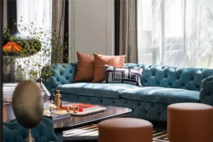 Modern living room featuring a blue tufted velvet sofa, brown leather pillows, and a wooden coffee table with books and a tea