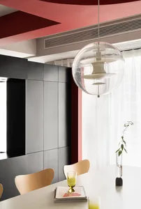 A modern kitchen with white countertops and wooden chairs, featuring a unique hanging light fixture and a vase with a plant.
