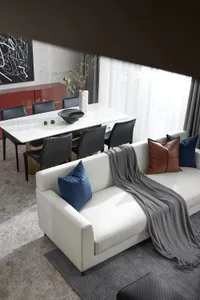 A modern minimalist living room with a white sofa, blue and brown pillows, and a grey throw blanket.