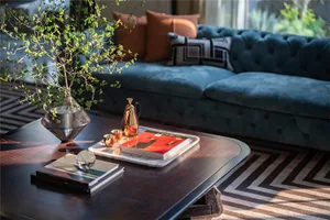 A modern living room with a blue tufted sofa, wooden coffee table, and decorative items.