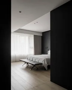 Modern minimalist bedroom featuring white walls and wooden floor, with a gray upholstered bench at the foot of the bed.