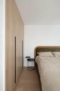 A minimalist bedroom with a wooden bed frame, side tables, and a wall-mounted wardrobe