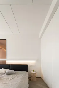 A minimalist bedroom featuring a black bed frame with a wooden headboard, grey bedding, and a wooden side table with a book a