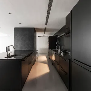 Interior view of a modern minimalist kitchen featuring black cabinets, metallic countertops, and stainless steel appliances.