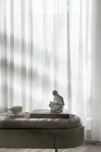 A serene interior space featuring a fabric curtain, a ceramic statue, a book, and a teacup with a saucer.
