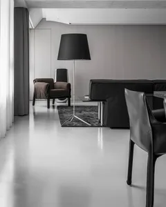 A minimalist living room with concrete flooring, a black sofa, a brown armchair, and a black floor lamp.