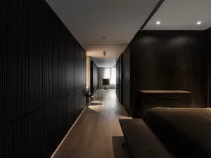 A modern minimalist bedroom with dark wood flooring, walls, and furniture.